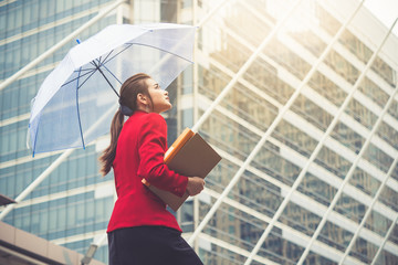 Young beautiful Asian business woman holding umbrella and documents walking to office for working under sunlight and hot weather. © Nattakorn