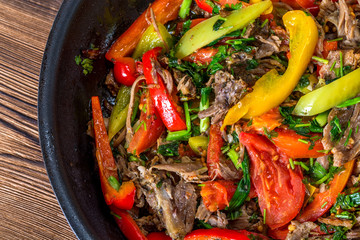 Meat with vegetables in a frying pan on a wooden background