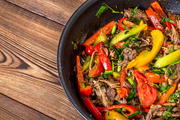 Meat with vegetables in a frying pan on a wooden background