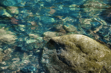 small multicolored stones on the bank of a mountain stream with crystal clear glacial water. Top view.
