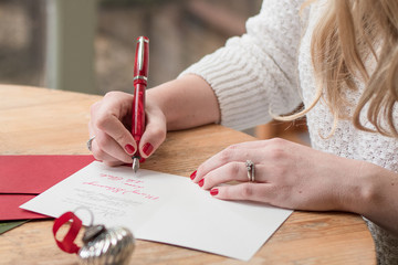 young woman writing christmas cards with red nails, a red pen, and holiday decorations