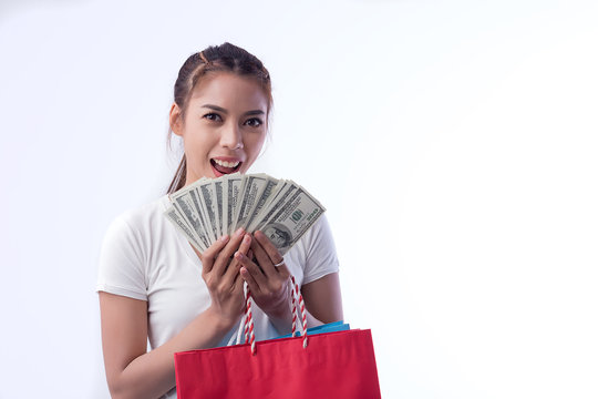 Picture of a beautiful black haired girl in a summer dress, holding a dollar bill with a shopping bag, and looking at the camera through a white background.