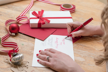 young woman writing christmas cards with red nails, a red pen, and holiday decorations