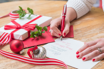 young woman writing christmas cards with red nails, a red pen, and holiday decorations