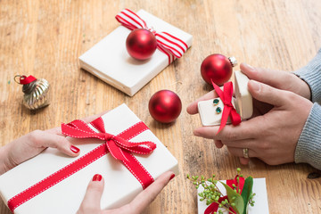 Romantic couple gives holiday Christmas gifts with red bows and Christmas deocorations on a wooden table