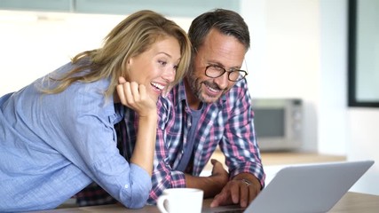 Mature couple connected with laptop at home - Powered by Adobe
