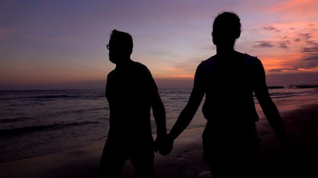 Couple walking on the beach and holding their hands, slow motion shot at 240fps, steadycam shot
