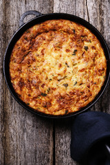 Zucchini, bacon and cheese casserole or gratin in cast-iron pan on vintage wooden table. Selective focus 