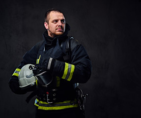 Firefighter dressed in uniform holds safety helmet.