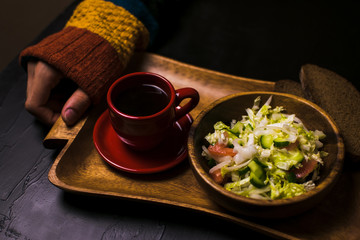 Man holding wooden tray with a salad and coffee on a black background