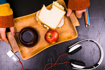 A man puts a wooden tray of food on a black background. Headphones, snack. Still life.