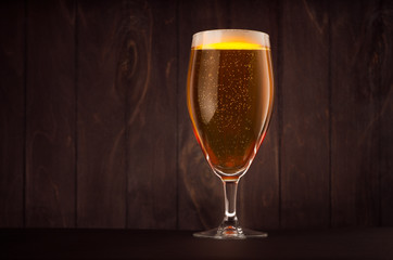Goblet beer glass with golden sparkling lager on dark wood board, copy space. Template for advertising, design, branding identity, restaurant menu, cover.