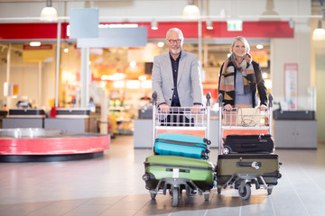 Happy Senior Business Couple With Luggage In Carts At Airport