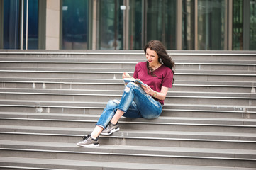 Obraz premium Beautiful woman reading a book on the steps of the building.