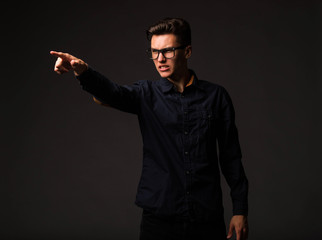 Young angry man portrait of a confident businessman showing by hands on a black background. Ideal for banners, registration forms, presentation, landings, presenting concept.