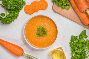Carrot soup with cream and parsley on white stone background. Top view. Copy space