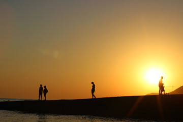 Fototapeta premium silhouette of people in the sun, sunset, silhouettes of people on the pier, evening walk