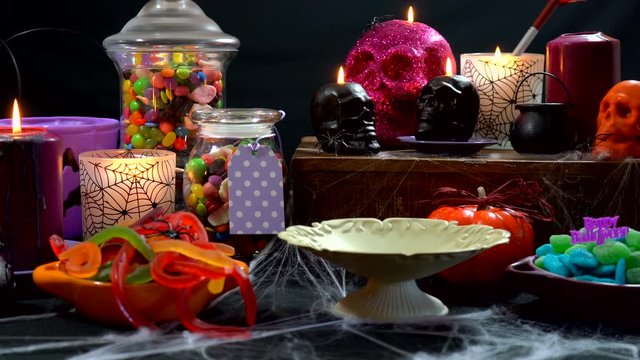 4k Happy Halloween trick or treat party table with bowls and apothecary jars of candy with skull candles against a black background, setting up table time lapse.