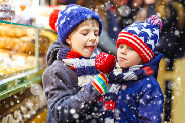 Two little kid boys eating sugar apple sweets stand on Christmas market