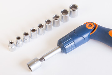 Top view of the screwdriver head. A set of heads and a screwdriver on a light background. Screwdriver with blue - orange bent handle and a set of heads under the nut.