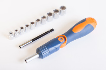 Top view of the screwdriver with the adapter. A set of heads and a screwdriver on a light background. Metal adapter for the nut. Screwdriver with blue - orange handle and a set of heads under the nut.