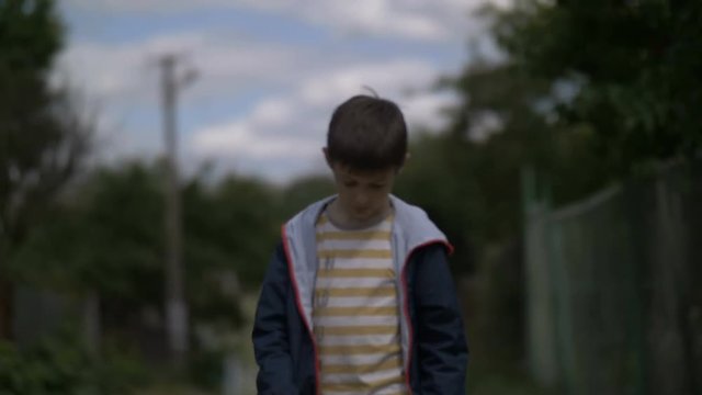 lonely sad boy walking along the village road with head down, ruffian naughty boy