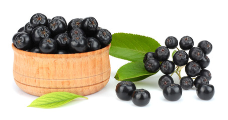 Chokeberry with leaf in wooden bowl isolated on white background. Black aronia