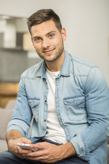 Smiling handsome man using smartphone sit in couch