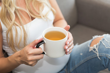 Pregnant long blond hair woman holds a mug of tea
