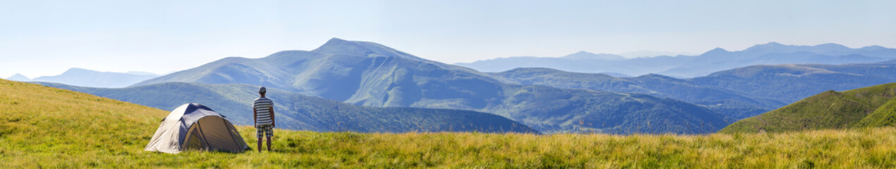 Hiker man standing near camping tent in carpathian mountains. Tourist enjoy mountain view. Travel...