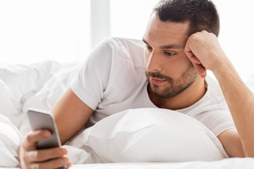 close up of man with smartphone in bed in morning