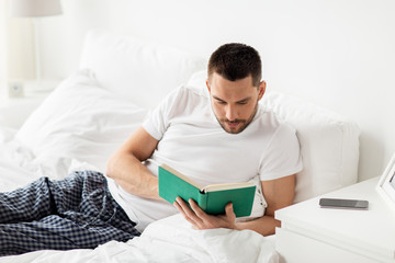 man reading book in bed at home