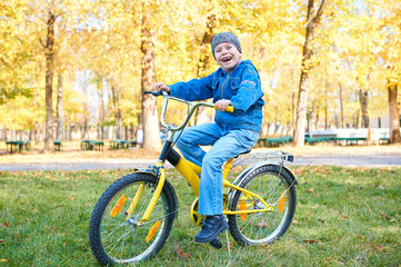 Fototapeta na wymiar boy riding on Bicycle in autumn Park, bright sunny day, fallen leaves on background