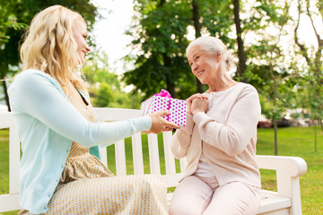 daughter giving present to senior mother at park