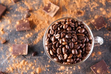 Full glass cup of Roasted coffee beans on the dark stone background with dissipate cocoa, pieces of chocolate and beans. Selective focus.Top view. Coffee love concept