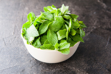 Fresh mint leaves in the ceramic bowl on the dark stone background. Healthy vegetarian food concept. Selective focus. Copy space for text.