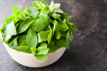 Fresh mint leaves in the ceramic bowl on the dark stone background. Healthy vegetarian food concept. Selective focus. Copy space for text.