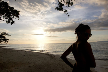 Fototapeta premium silhouette of young woman by the sea with sun glasses at sunset