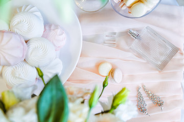 Bridal morning details composition. Top view of bride's jewelery, perfumes, bouquet of eustoma flowers and marshmallow and macaroon sweets. Flat lay. Selective focus. Space for text.