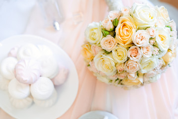 Wedding details. Top view of bride's bouquet of light roses flowers on the table with perfumes and arshmallow sweets. Flat lay. Selective focus. Space for text.