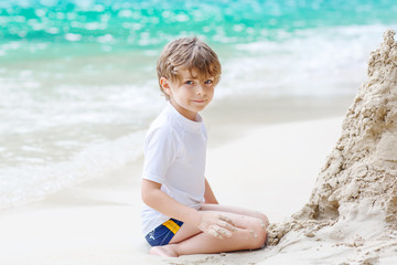 Little kid boy building sand castle on tropical beach