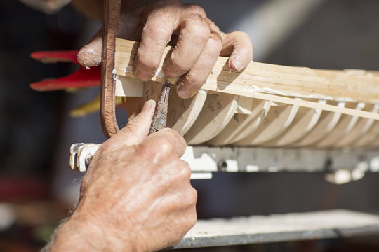 handcrafted craftwork of a wooden boat model / old man working on creating a wooden model of a boat  
