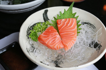 Salmon raw slice or salmon sashimi in Japanese style fresh serve on ice with fresh wasabi on black table.