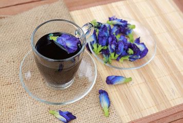 Obraz na płótnie Canvas Butterfly pea juice in transparent glass and flowers on sack - wood mat background.