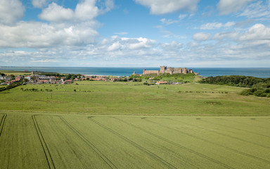 Obraz premium Bamburgh village and Castle, England. A drone view of the Northumberland landmark on the coast between the English countryside and the North Sea.