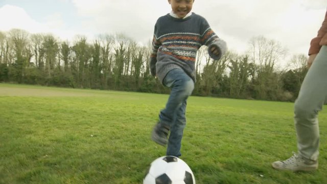 Happy young Asian father and son playing football outdoors and having fun