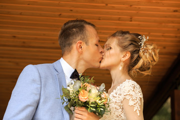Portrait of young groom and beautiful bride with a wedding bouquet. The newlyweds are posing near the house.