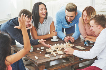 Group of creative friends sitting at wooden table. People having fun while playing board game