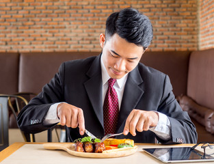 Young asian businessman in formal suit feeling hungry, eating many foods on table at cafe