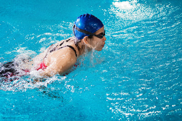 Swimmers are swimming "butterfly" poolside at night.